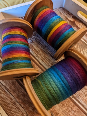 Three bobbins of colourful single spun yarn
